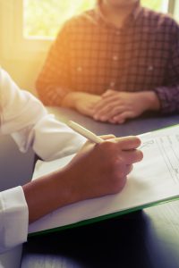 Asian Female Doctor Sitting At Hospital Office Desk Giving All P