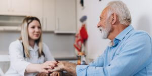 Young Positive Caregiver Taking Care Of Senior Man In Nursing Ho
