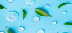 Cosmetics Gel And Green Leaves On Blue Background. Texture Of Bl